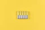 Photo of five grey-yellow alkaline AA batteries on a yellow background.