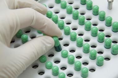Close-up image showing a gloved hand removing a green pill from a pill tray