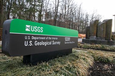A street sign for the US Geological Survey building with an artwork of basalt columns behind.