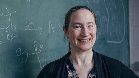 Melanie Sanford with a green chalkboard and chemistry symbols